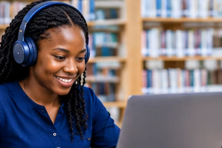 A learner with headphones studying on a laptop in a library